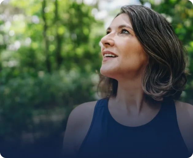 Woman smiling outdoors in natural sunlight with green foliage background